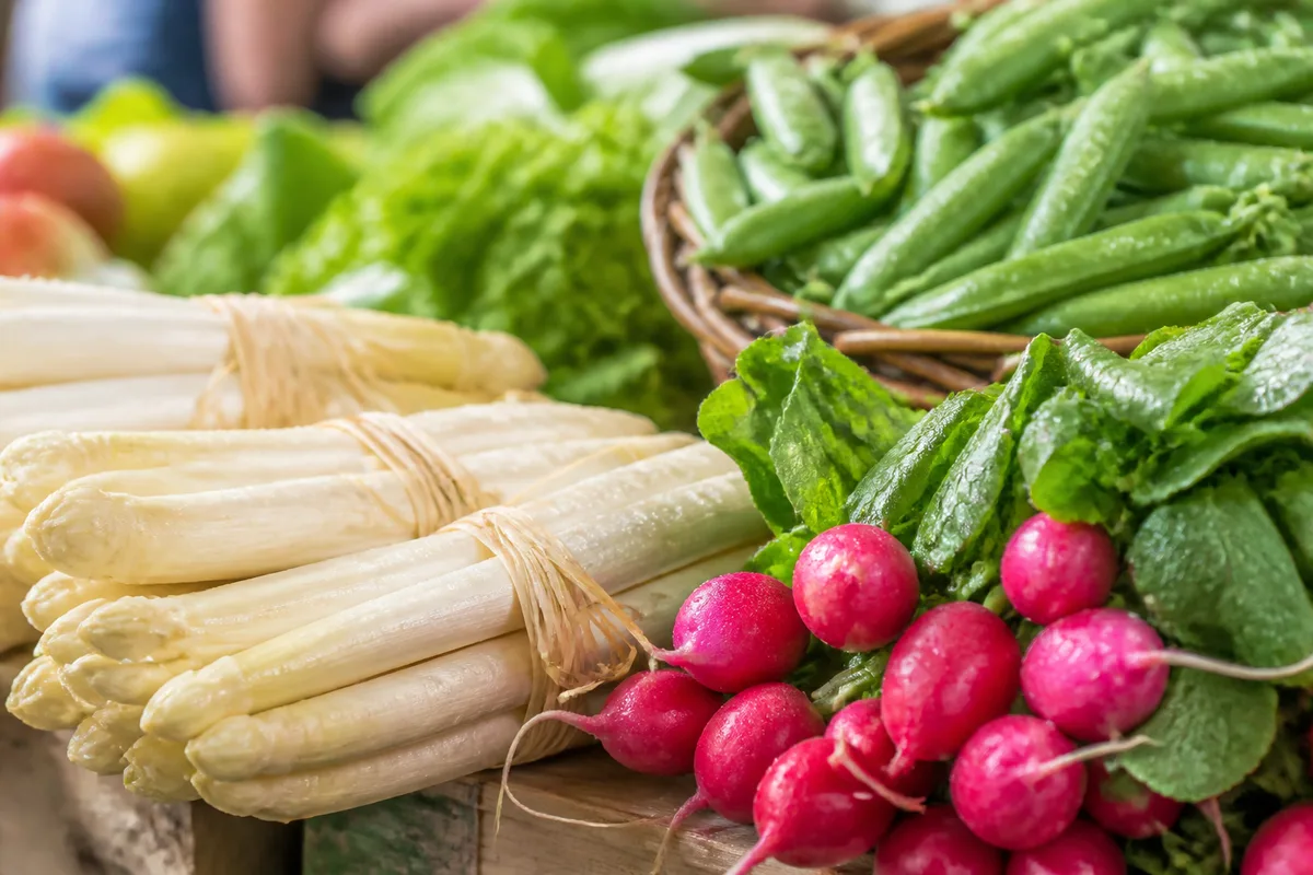 Étal de marché au printemps avec bottes d’asperges blanches, radis roses et petits pois frais